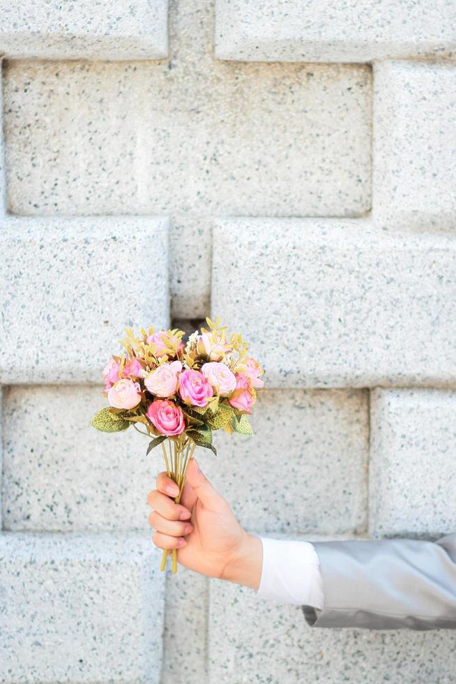 brudgum innehav en bukett av rosa reste sig blommor och betong vägg bakgrund. valentine dag för kärlek och firande begrepp. foto