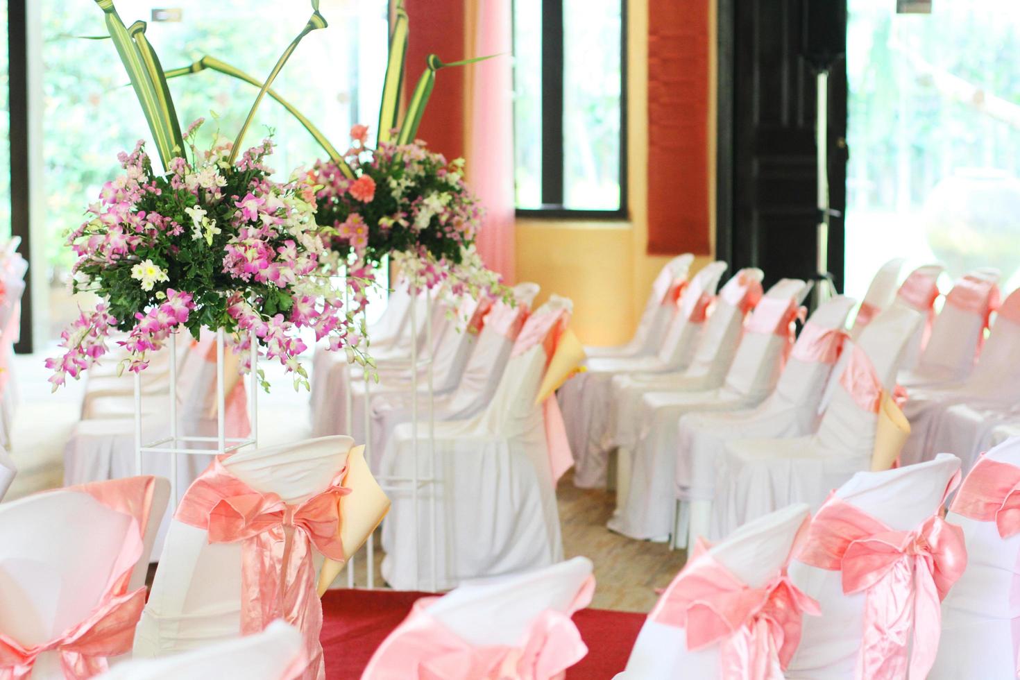 skön stolar dekoration med rosa band och bukett av orkidéer med blommor i en vas i bröllop händelse hall. foto