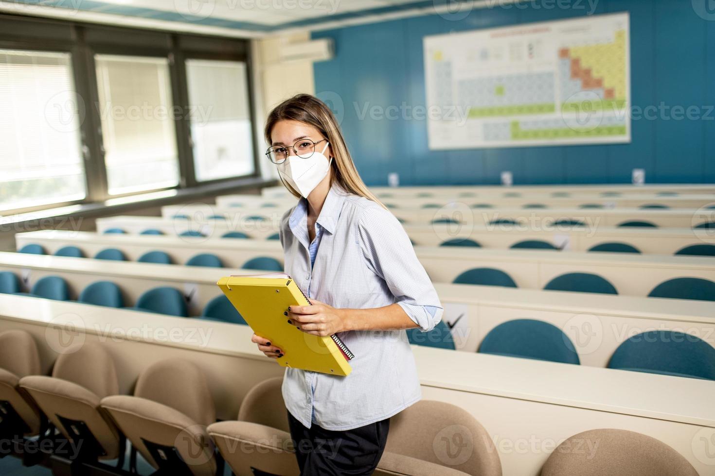 kvinnlig student som bär ansiktsskyddande medicinsk mask för virusskydd som står vid föreläsningssalen foto
