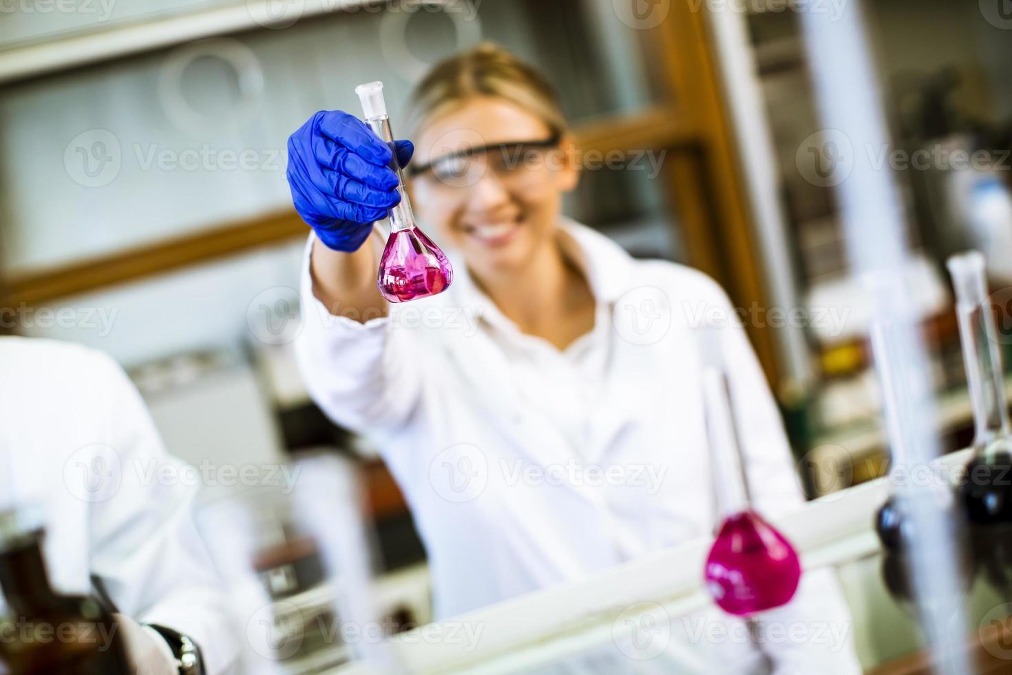 ung kvinnlig forskare som undersöker vätska i biokemiskt laboratorium foto