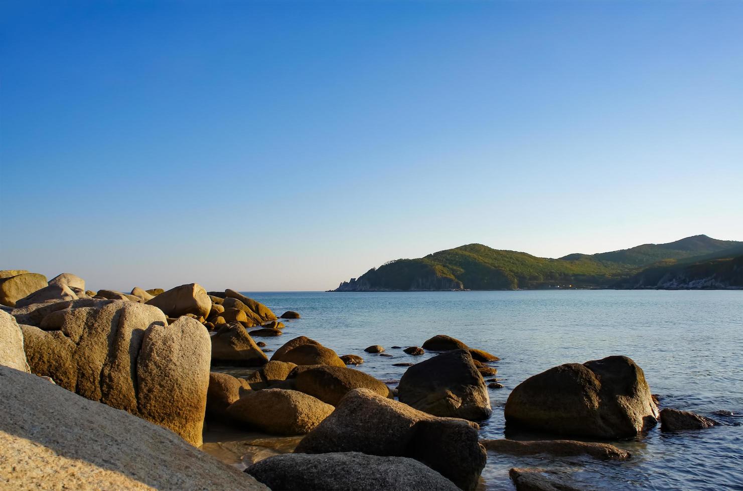 marinmålning med stenar på stranden och berg i bakgrunden vid Japans hav foto