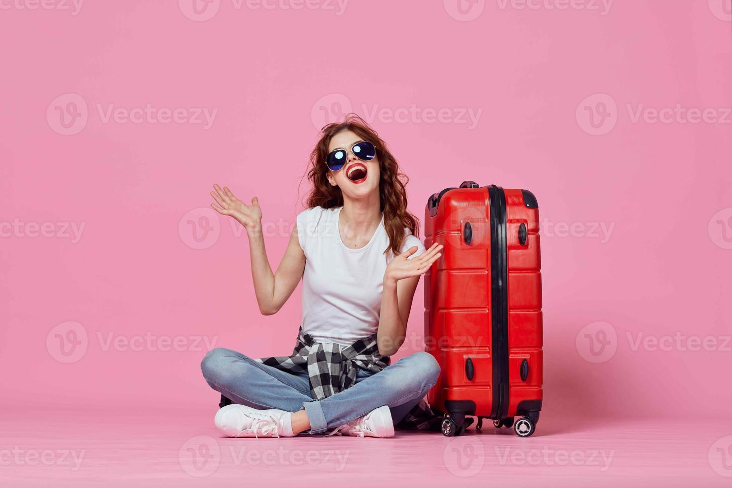 glad Söt kvinna med röd resväska pass och plan biljett resa rosa bakgrund foto