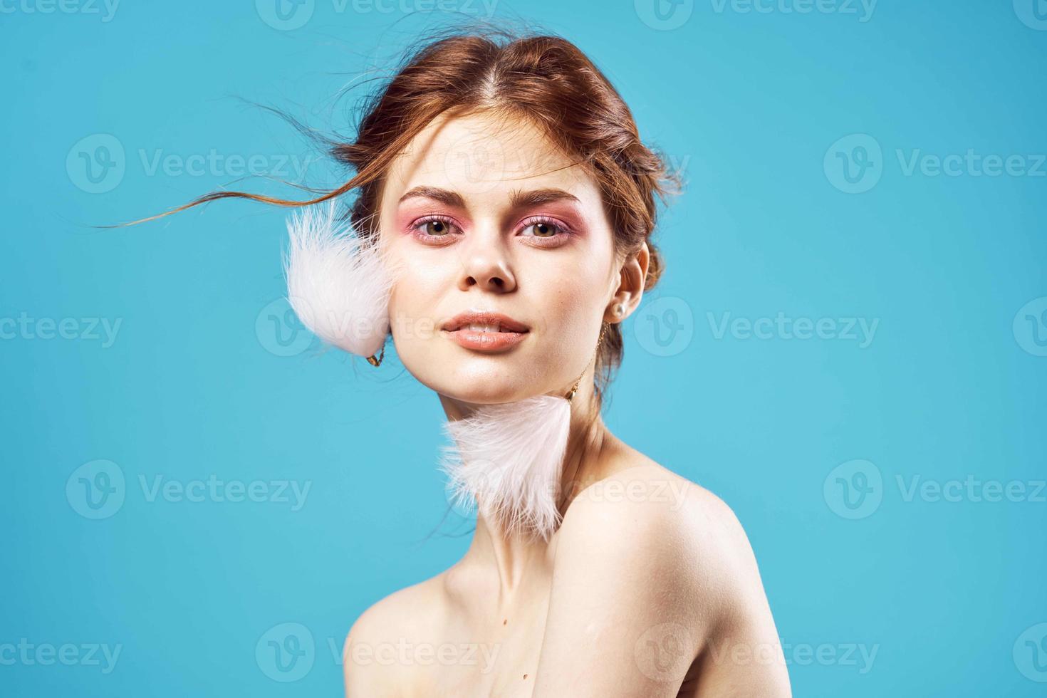kvinna med ljus smink på naken axlar och fluffig örhängen mode blå bakgrund närbild foto
