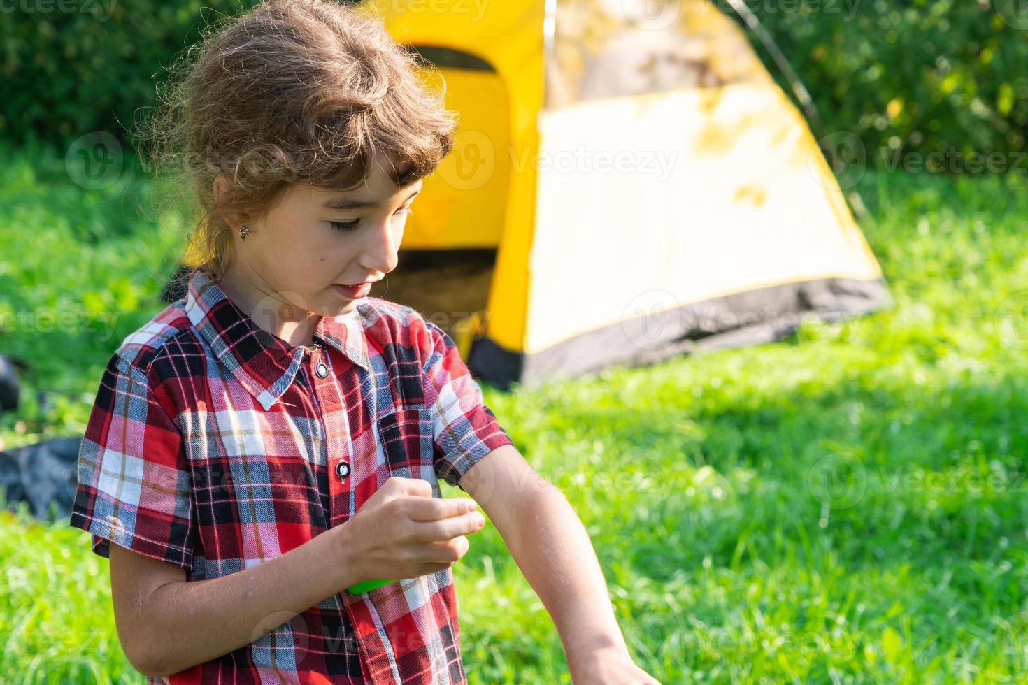 flicka sprayar myggspray på huden i naturen som biter hennes händer och fötter. skydd mot insektsbett, avstötande säkert för barn. friluftsliv, mot allergier. sommartid foto