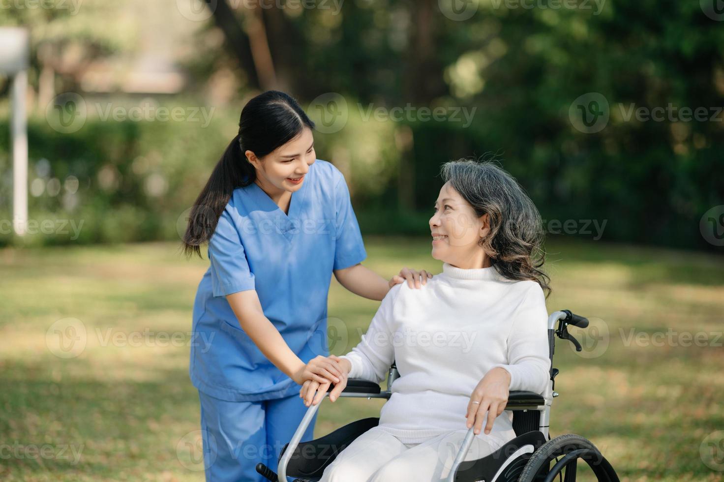 äldre asiatisk senior kvinna på rullstol med asiatisk försiktig vårdgivare och uppmuntra patient, gående i trädgård. med vård från en vårdgivare och senior hälsa försäkring. foto