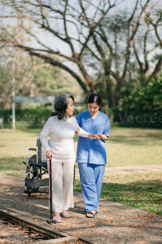 äldre asiatisk senior kvinna på rullstol med asiatisk försiktig vårdgivare. amning Hem sjukhus trädgård begrepp. foto