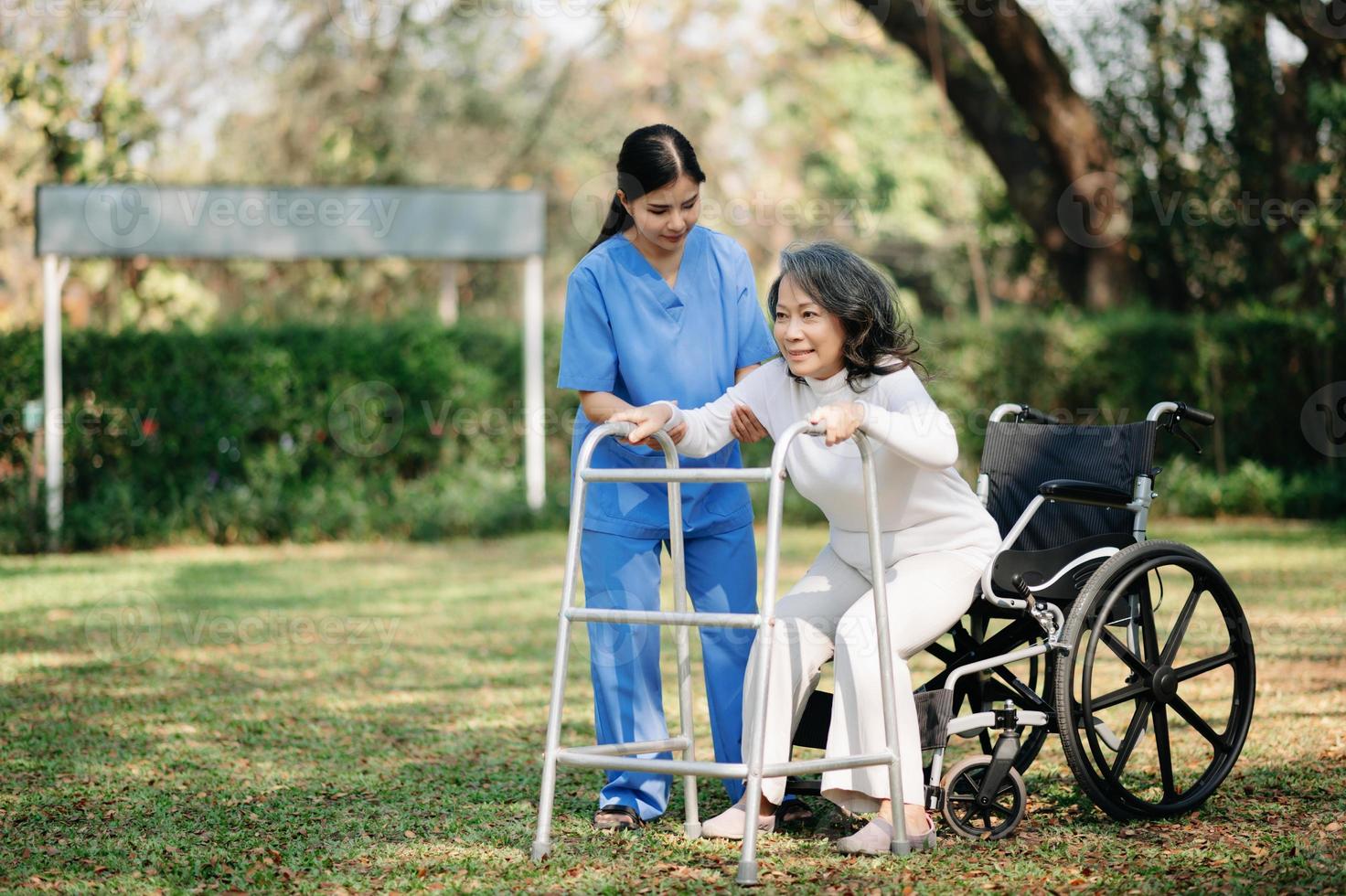 asiatisk försiktig vårdgivare eller sjuksköterska och de Lycklig patient i en rullstol är gående i de trädgård till hjälp och uppmuntra och resten din sinne med grön natur. hjälp Stöd själv till lära sig till promenad. foto