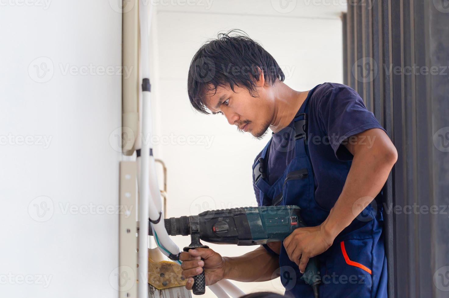 man med hammare borra framställning hål i vägg, tekniker man montera ett luft konditionering i en klient hus, ung reparatör fixering luft balsam enhet, underhåll och reparation begrepp foto