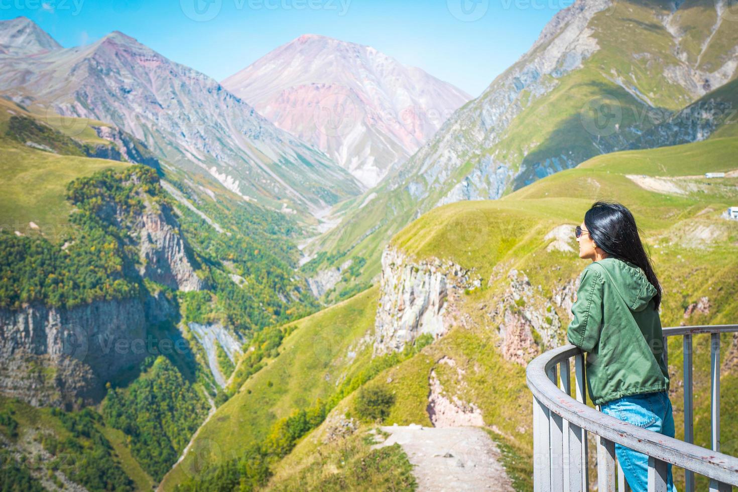 kvinnlig kvinna står på gudauri utsiktsplats plattform och ser till natursköna bergslandskap av kazbegi. resmål i georgien foto