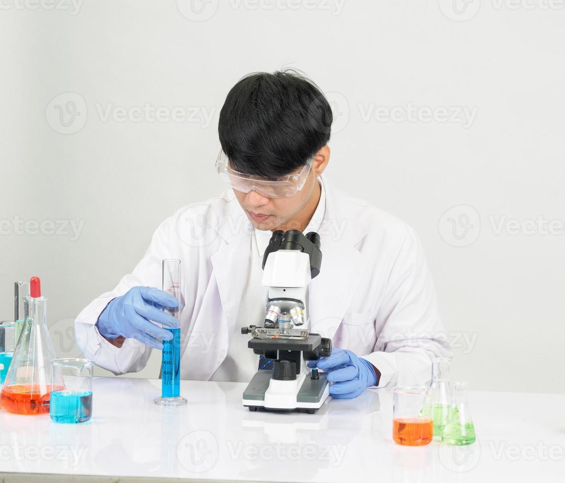 asiatisk manlig studerande forskare bär en läkares klänning i de labb ser hand på kemist. orsakade förbi blandning reagens i vetenskaplig forskning laboratorier med testa rör och mikroskop på de tabell foto