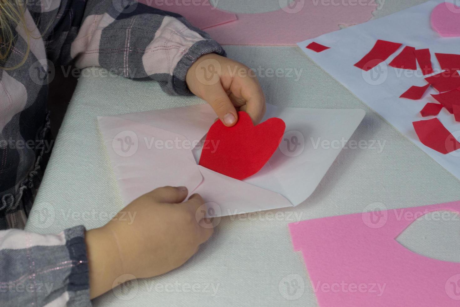 barn innehav brev med röd papper hjärtkärlek brev för hjärtans dag, gåva för mödrar dag, lilla flicka sätta handgjort hjärta inuti kuvert, semester hälsningar från dotter, håna upp för kärlek lyckönskningar foto