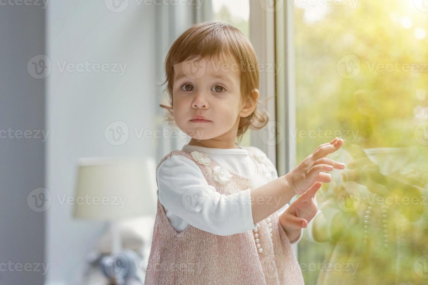 liten flicka stående på fönster tröskel foto