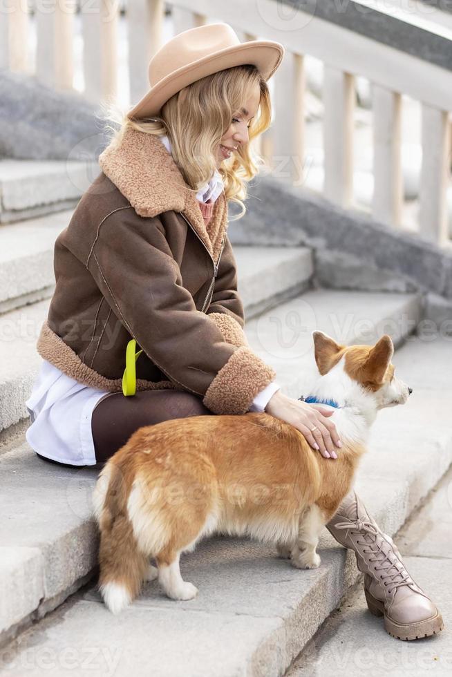 en ung blond kvinna i en hatt på en promenad i de parkera med welsh corgi-pembroke hundar.vår foto