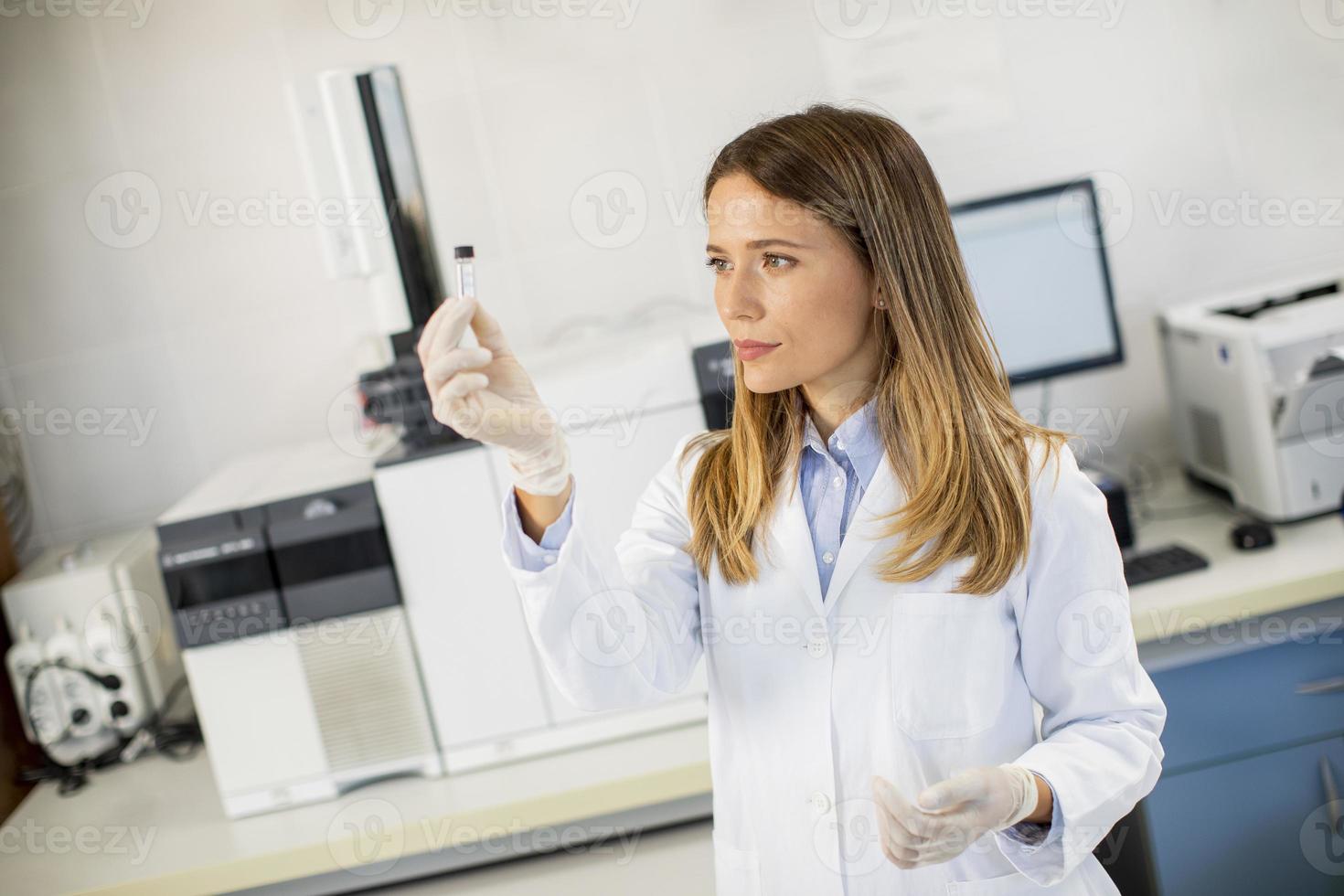 kvinnlig forskare i en vit labrock förbereder flaskan med ett prov för en analys på en gaskromatograf i biomedicinskt laboratorium foto