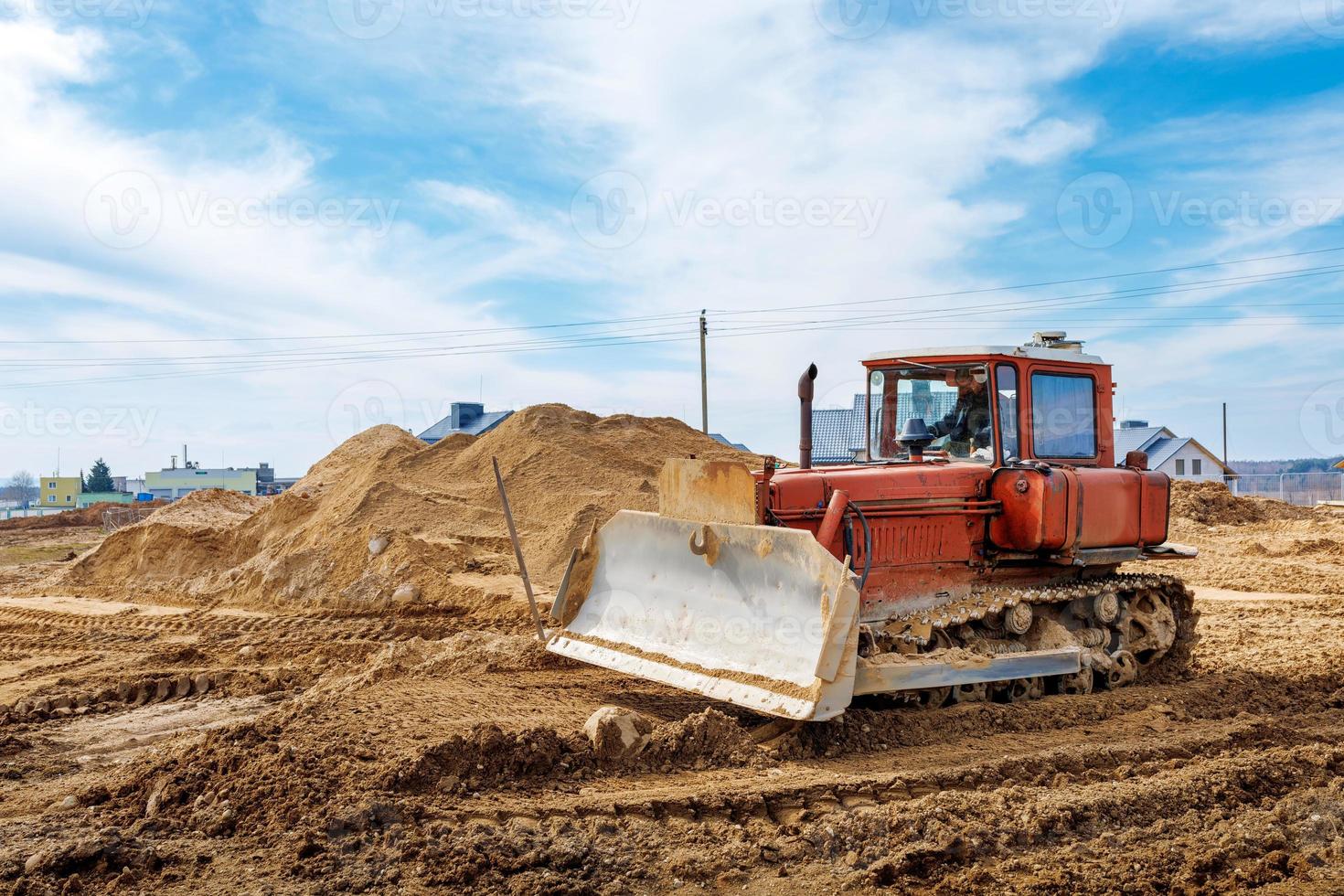 ett gammal orange bulldozer utför arbete till nivå de sandig jord foto