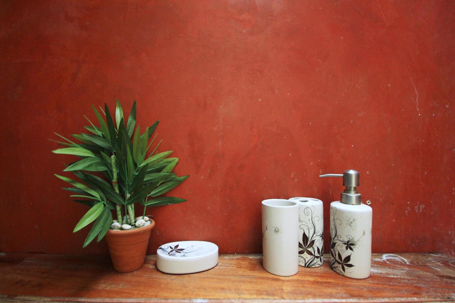 växt i lera pott med schampo, tvål och dusch grädde flaska på trä- skåp nära orange vägg dekoration i badrum årgång stil foto