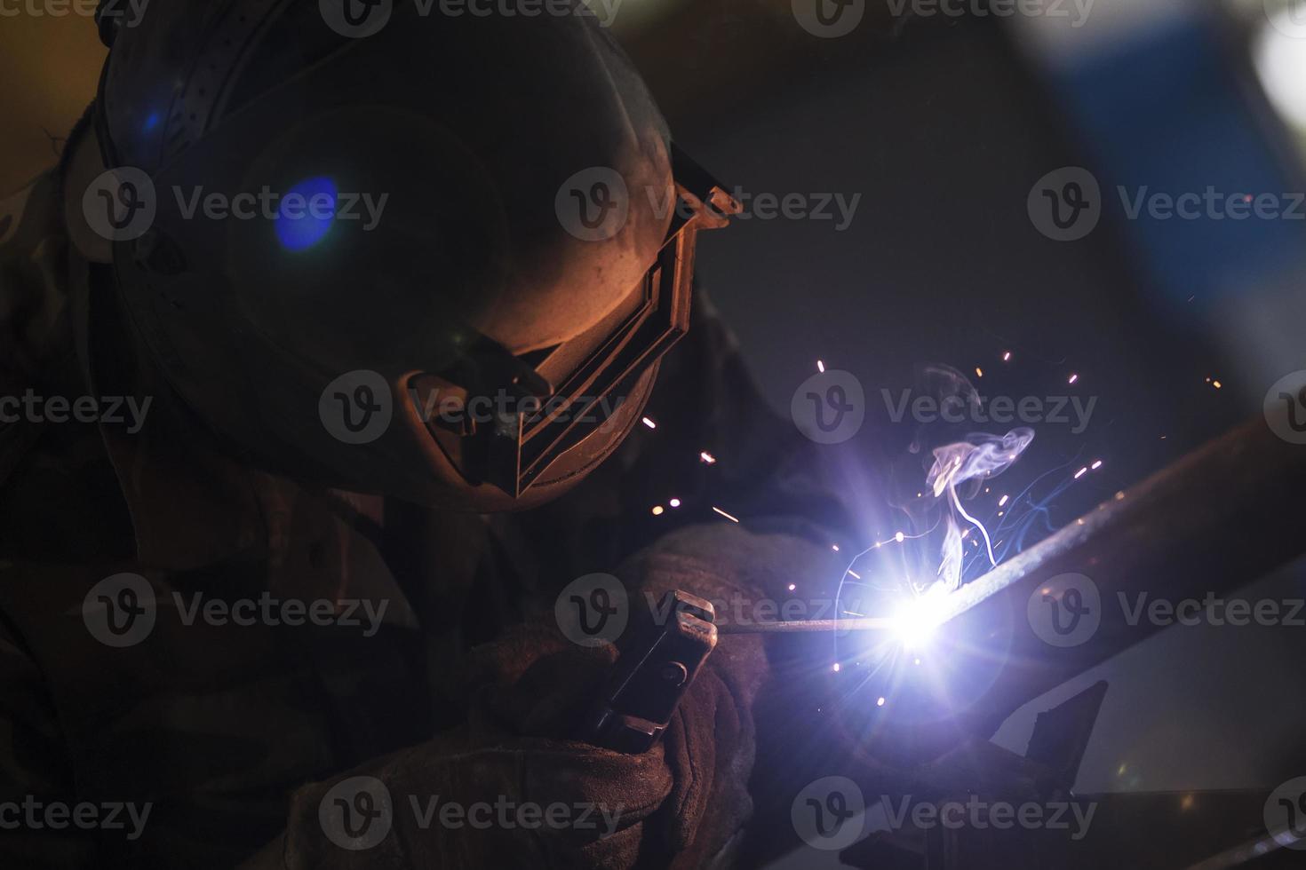 svetsare på arbete. man i en skyddande mask. de svetsare gör sömmar på de metall. gnistor och rök när svetsning. foto