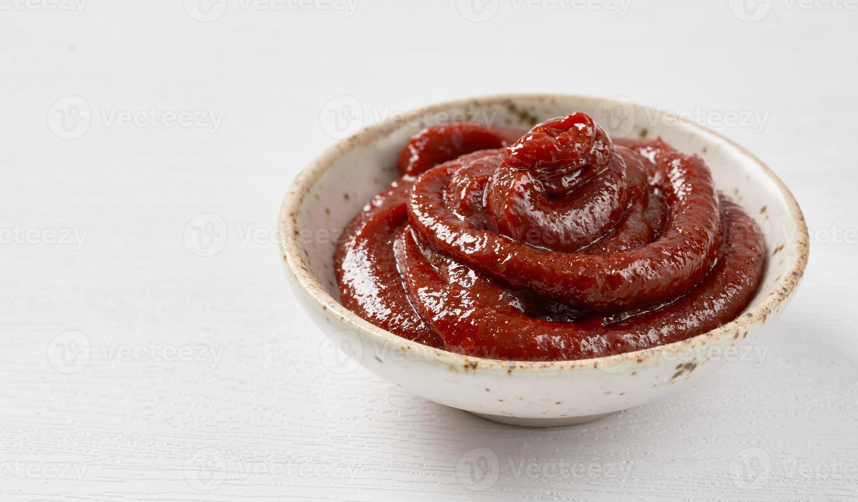 gochujang eller koreanska röd chili klistra i en keramisk skål på vit trä bakgrund. röd chili sås gochujang krydda foto