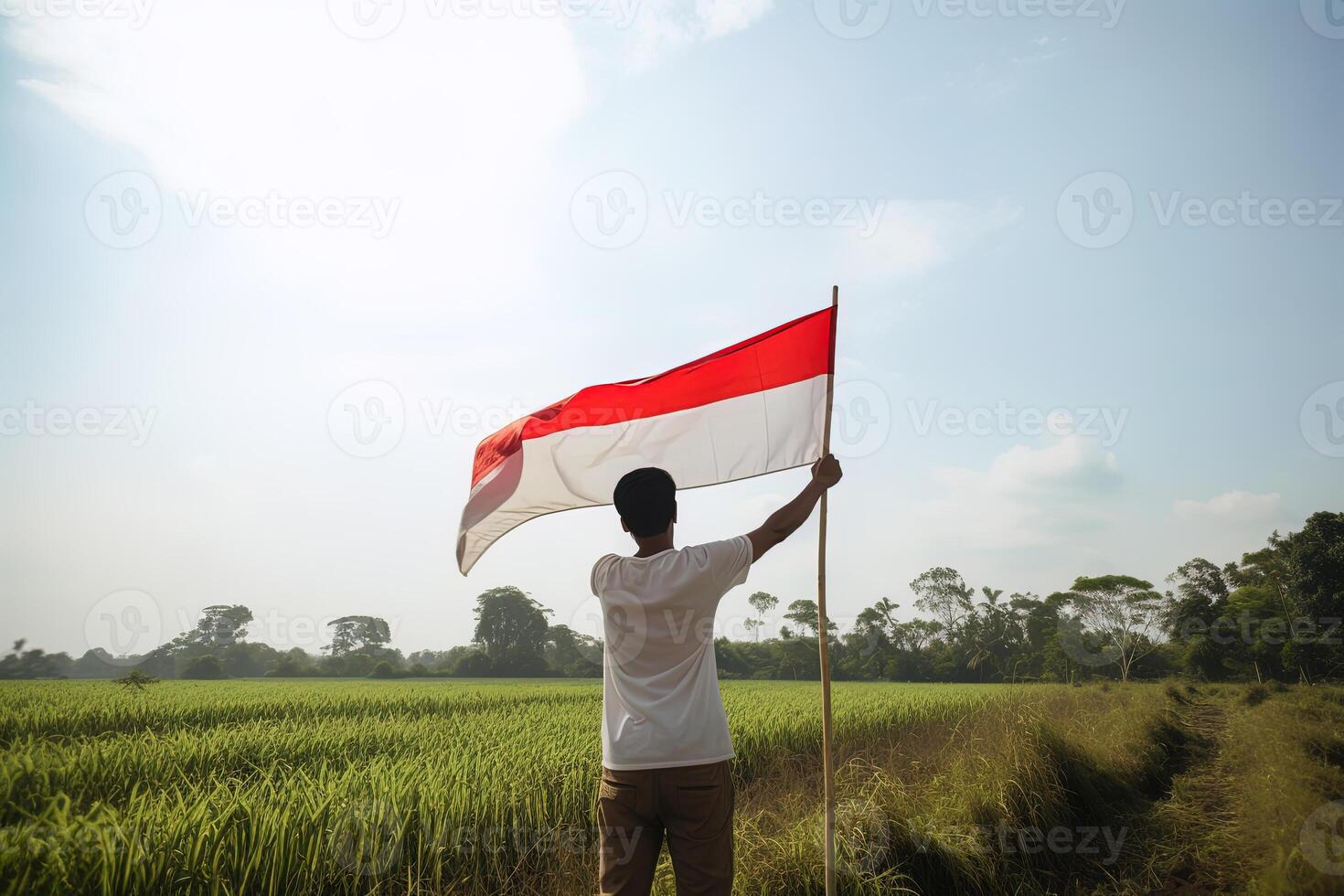 en man innehav en röd och vit indonesien flagga på topp av en frodig grön ris fält. ai genererad foto