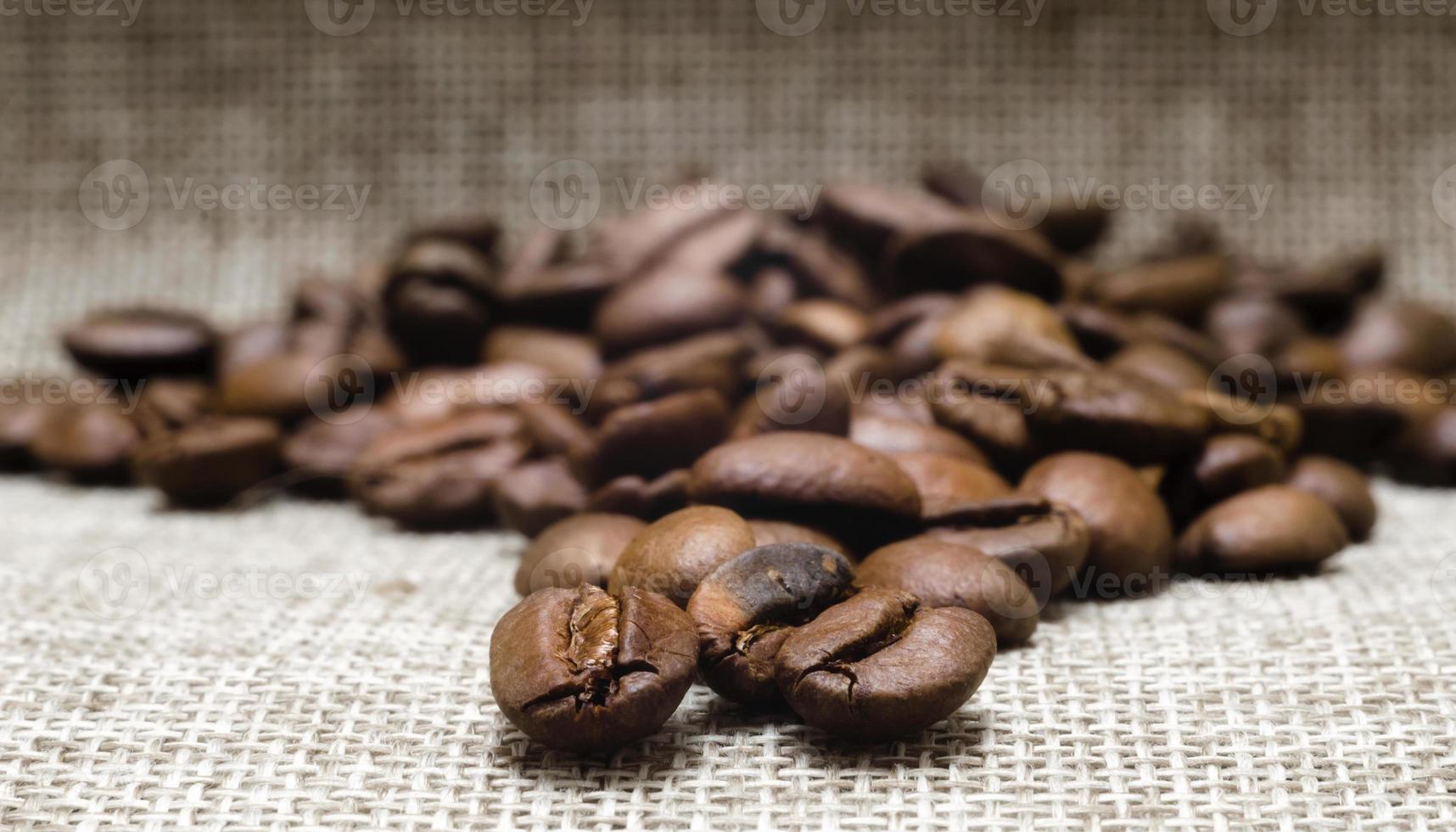 hög av rostade kaffebönor på en mattmakro, beige bakgrundsslut upp foto