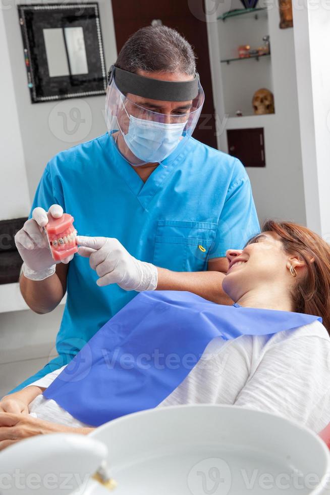 skön kvinna tar emot förklaringar handla om henne dental behandling med henne tandläkare. läkare använder sig av en dental modell. foto