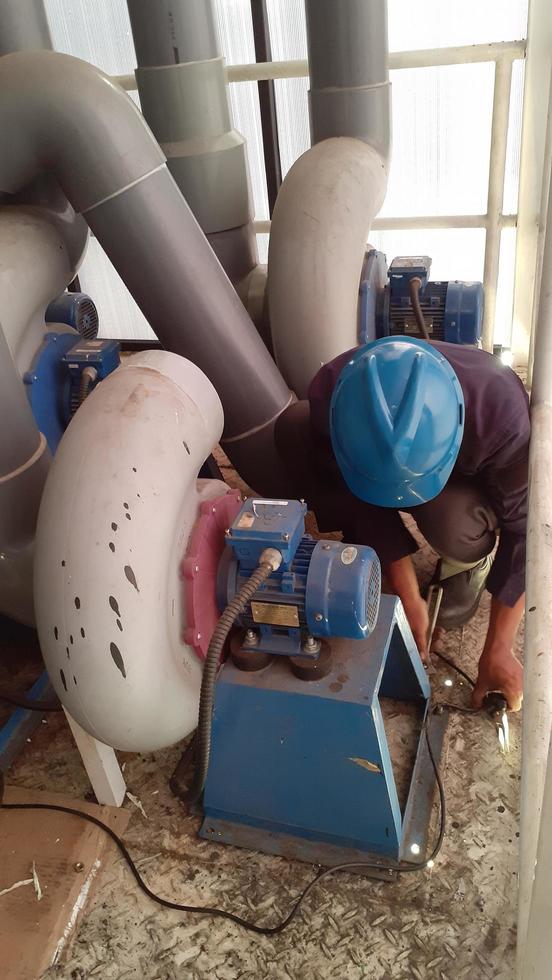 jakarta indonesien april 2023 en arbetstagare i en skyddande hjälm och säkerhet skor reparation en pump blåsare. foto