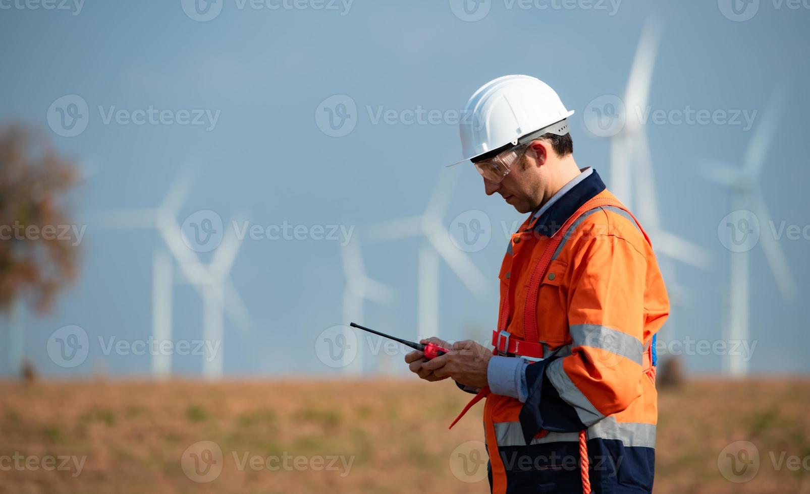 ingenjör på naturlig energi vind turbin webbplats med en uppdrag till ta vård av stor vind turbiner använda sig av en walkie prat till kommunicera med en kollega arbetssätt på topp av de vind turbin. foto