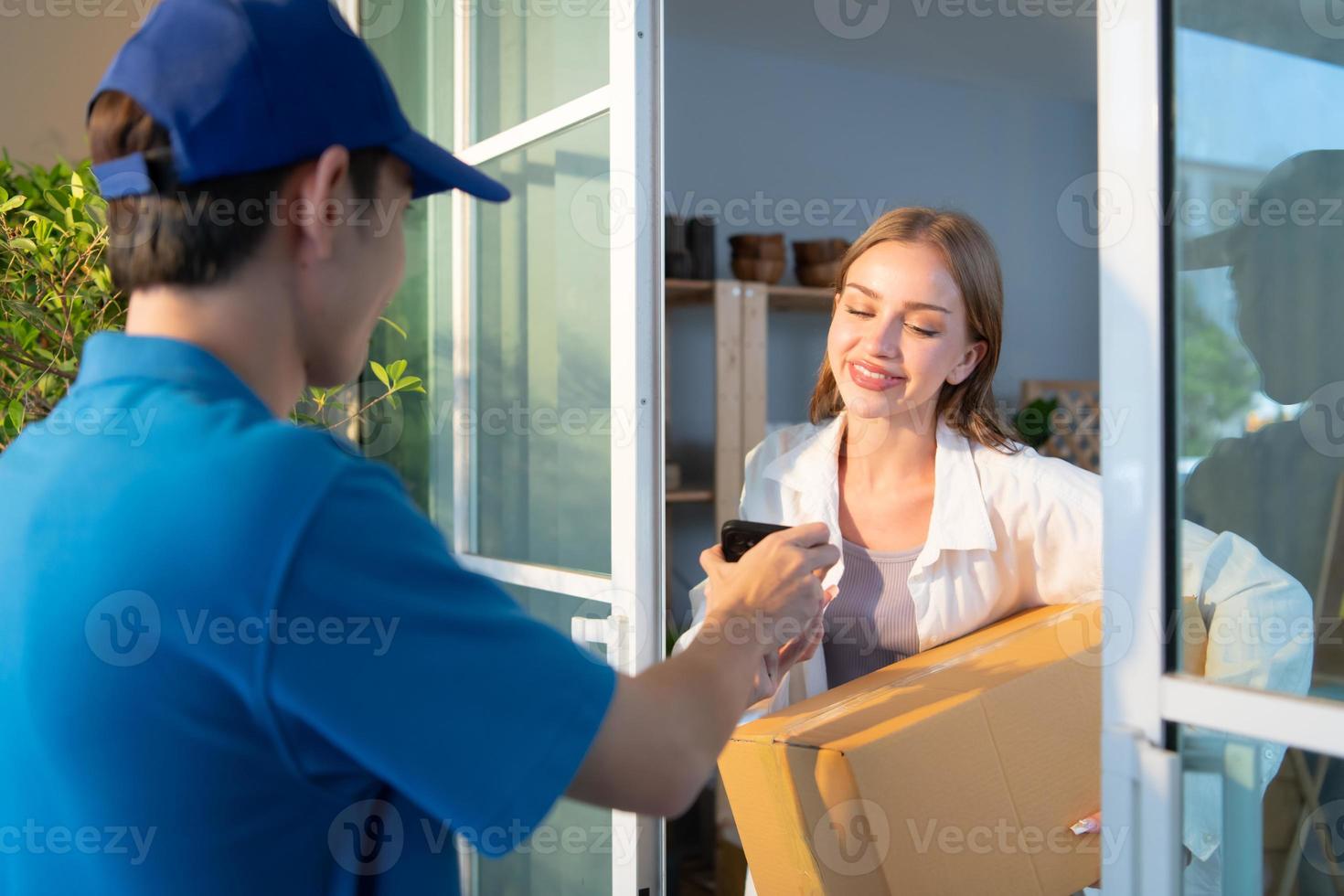 ung kvinna tecken henne namn på en smartphone efter tar emot en låda av objekt från de leverans person. foto