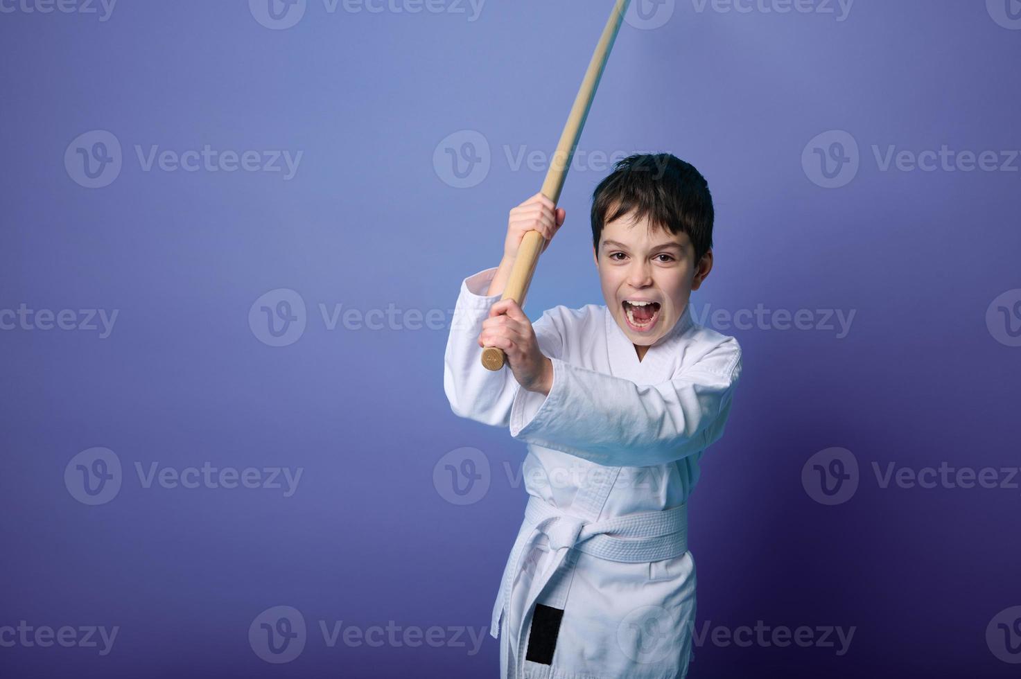 porträtt av en barn pojke aikido brottare bär traditionell samuraj hakama kimono inlärning bekämpa med bambu bokken. aikido inlärning begrepp foto