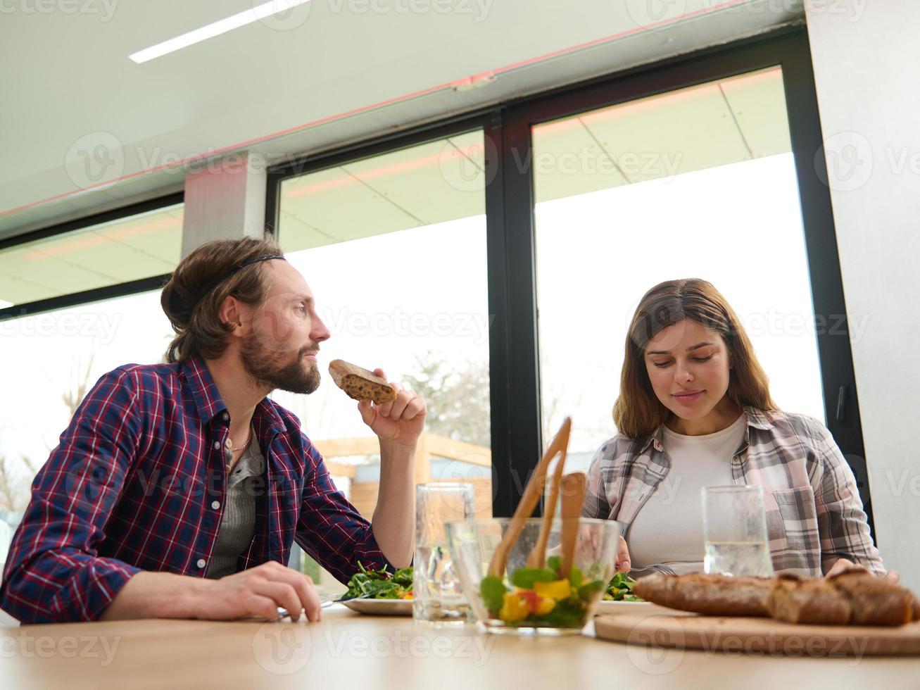 stilig caucasian man och kvinna, Make och fru, skön par har roligt talande på Hem över en utsökt lunch Sammanträde på tabell mot fönster utsikt de trädgård foto