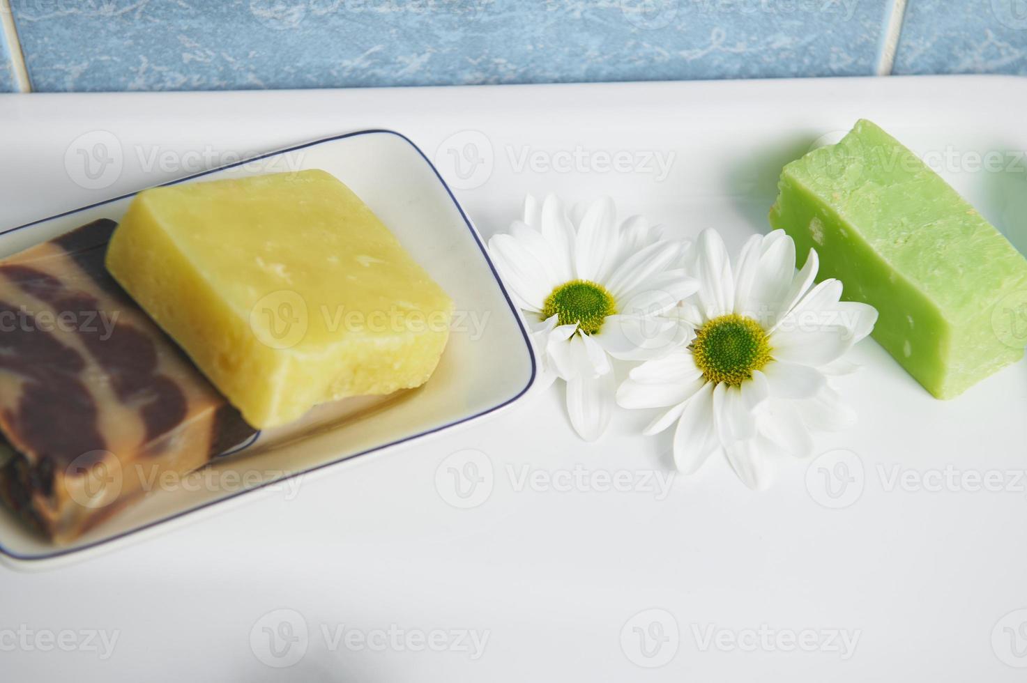 selektiv fokus på kamomill blommor och handgjorda tvål barer med naturlig ört- Ingredienser på vit keramisk tvätta handfat foto