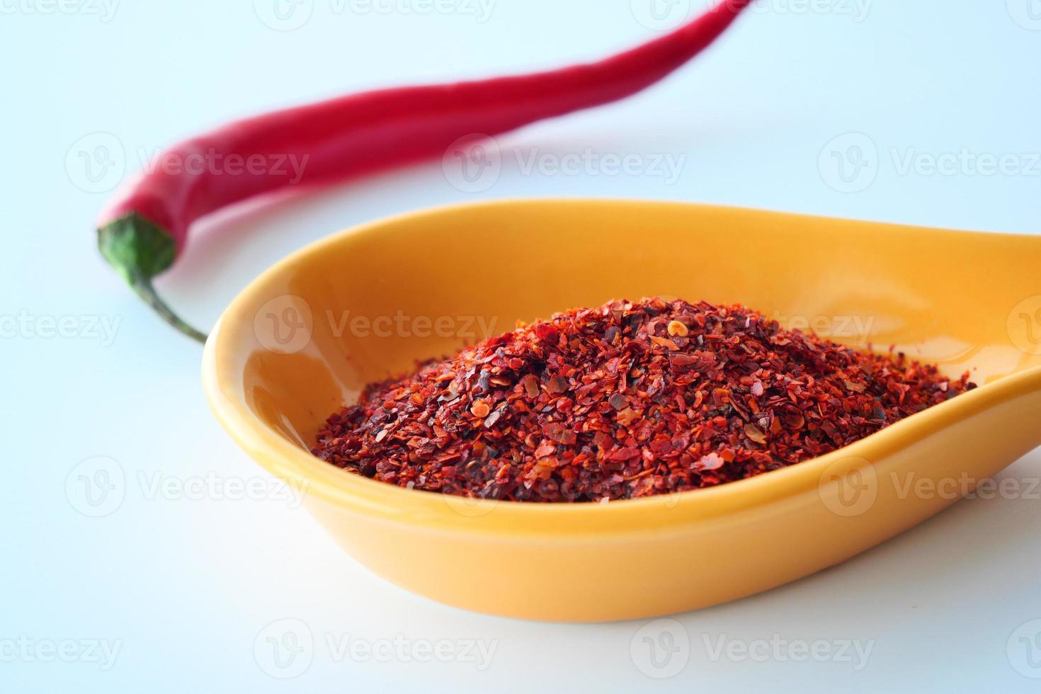 röd chili flingor eller pulver i en sked på vit foto