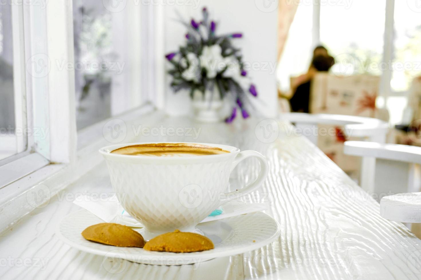 varm latte kaffe i en vit kaffe kopp med småkakor på vit trä- tabell. foto