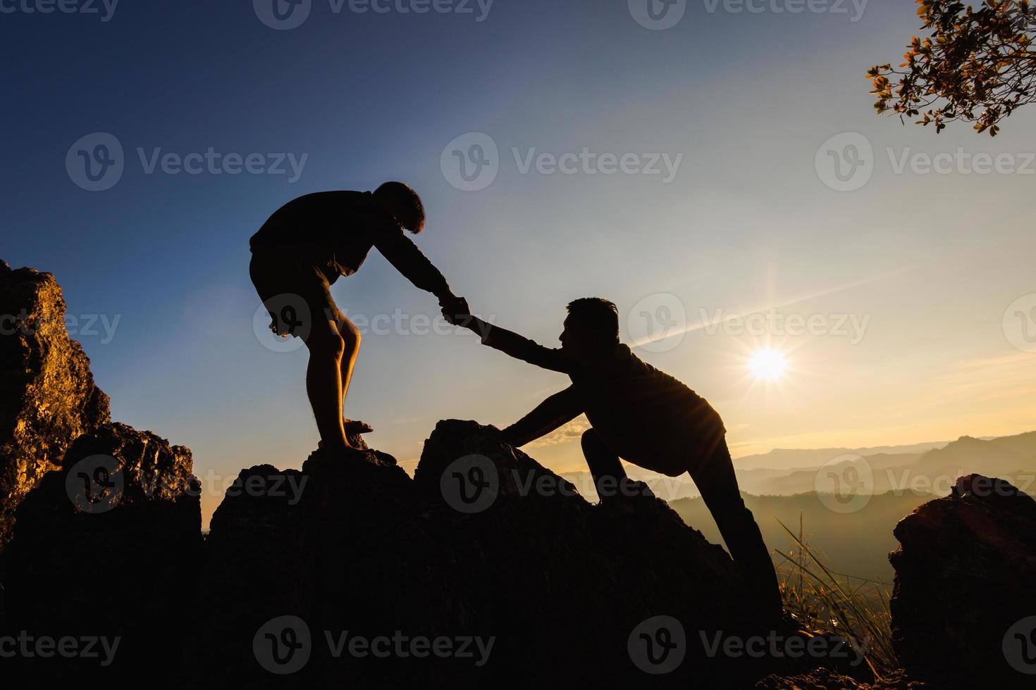 silhuetter av två människor klättrande på berg och portion. hjälp och bistånd begrepp. foto