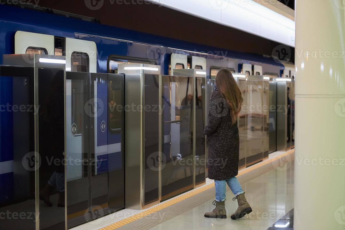 en flicka i en kirurgisk ansiktsmask håller socialt avstånd på en tunnelbanestation foto