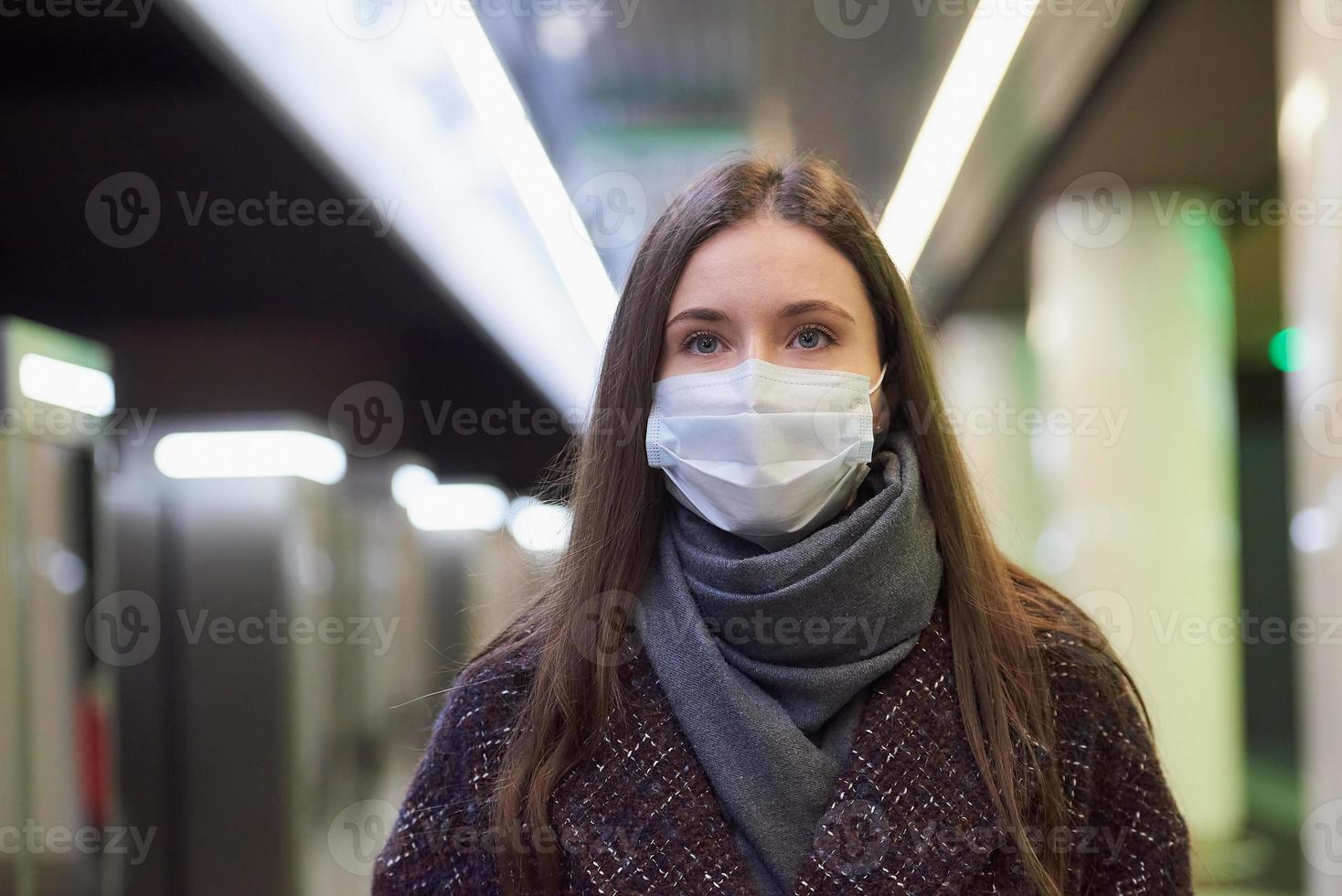 en kvinna i en medicinsk ansiktsmask väntar på ett ankommande tåg på tunnelbanan foto