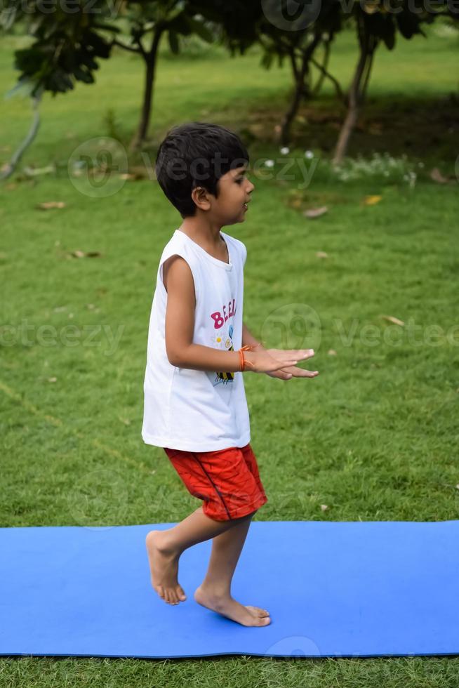 asiatisk smart unge håller på med yoga utgör i de samhälle parkera utomhus, barns yoga utgör. de liten pojke håller på med yoga träning. foto