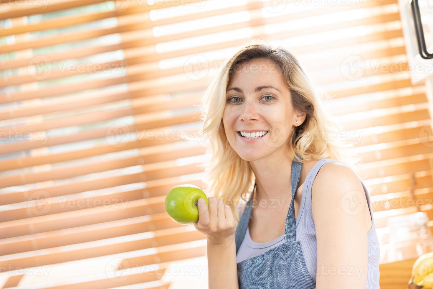 Lycklig friska passa kvinna med grön äpple på Hem kök. diet eller näring mat med kopia Plats. skön kvinna stå med Lycklig ansikte, njut av äter äpple, friska livsmedel för hälsa vård friskvård. foto