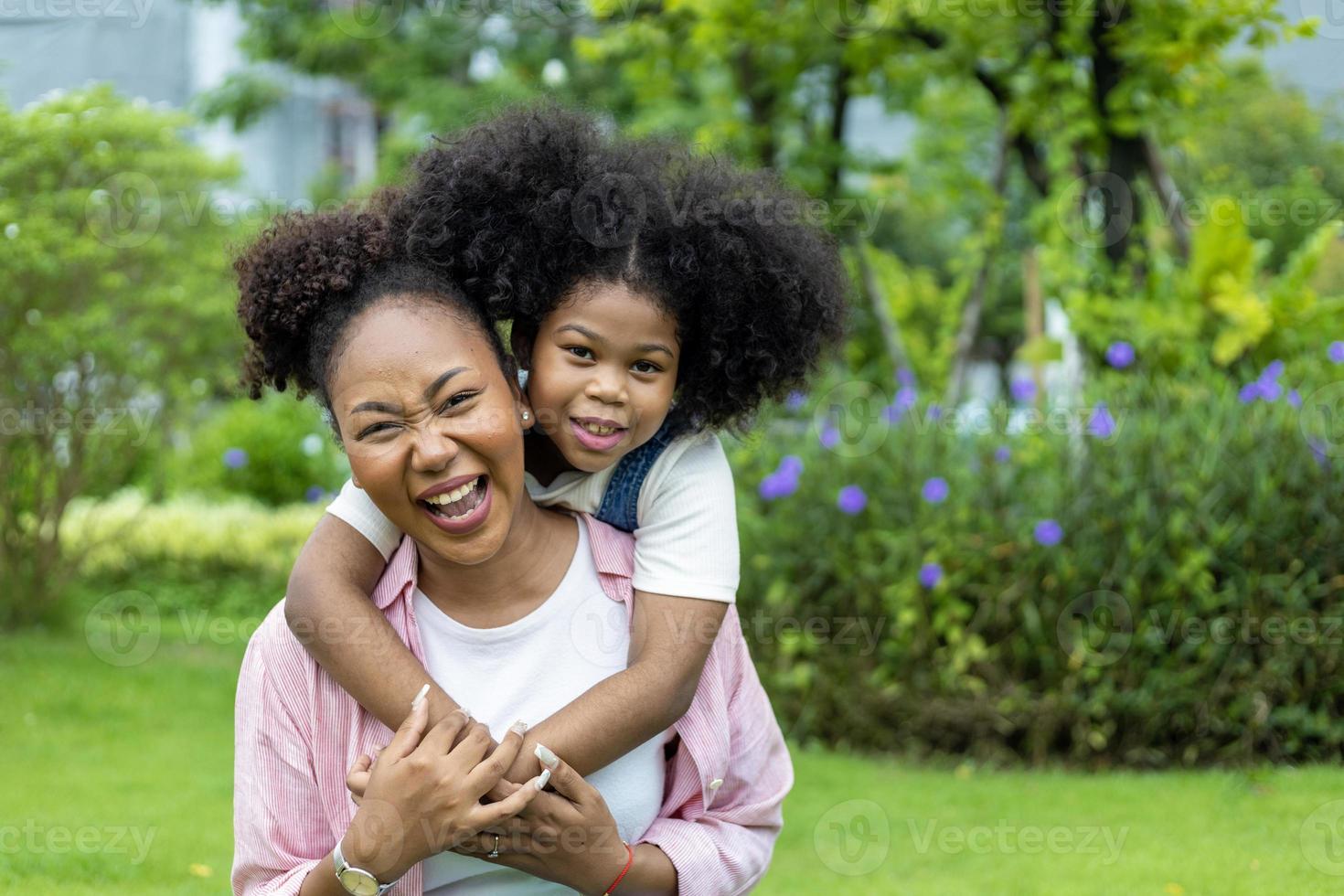 afrikansk amerikan mor är spelar piggyback ridning och kramas med henne ung dotter medan har en sommar picknick i de offentlig parkera för välbefinnande och lycka begrepp foto