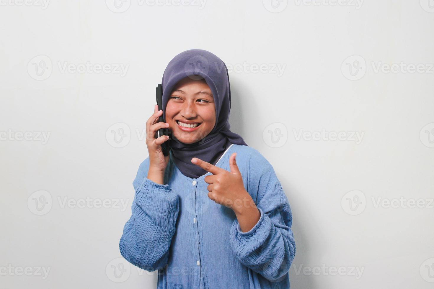 ung asiatisk flicka i hijab gör en telefon ring upp medan pekande fingrar åt sidan foto