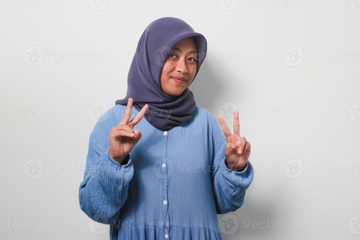 ung asiatisk flicka i hijab håller på med fred symbol isolerat över vit bakgrund. foto