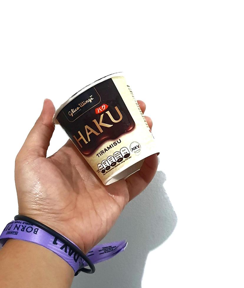 jakarta, indonesien i Mars 2023. isolerat vit Foto av en hand med en lila svartrosa konsert handledsband armband innehav en haku is grädde, ett av de is grädde Produkter produceras förbi glico vingar.
