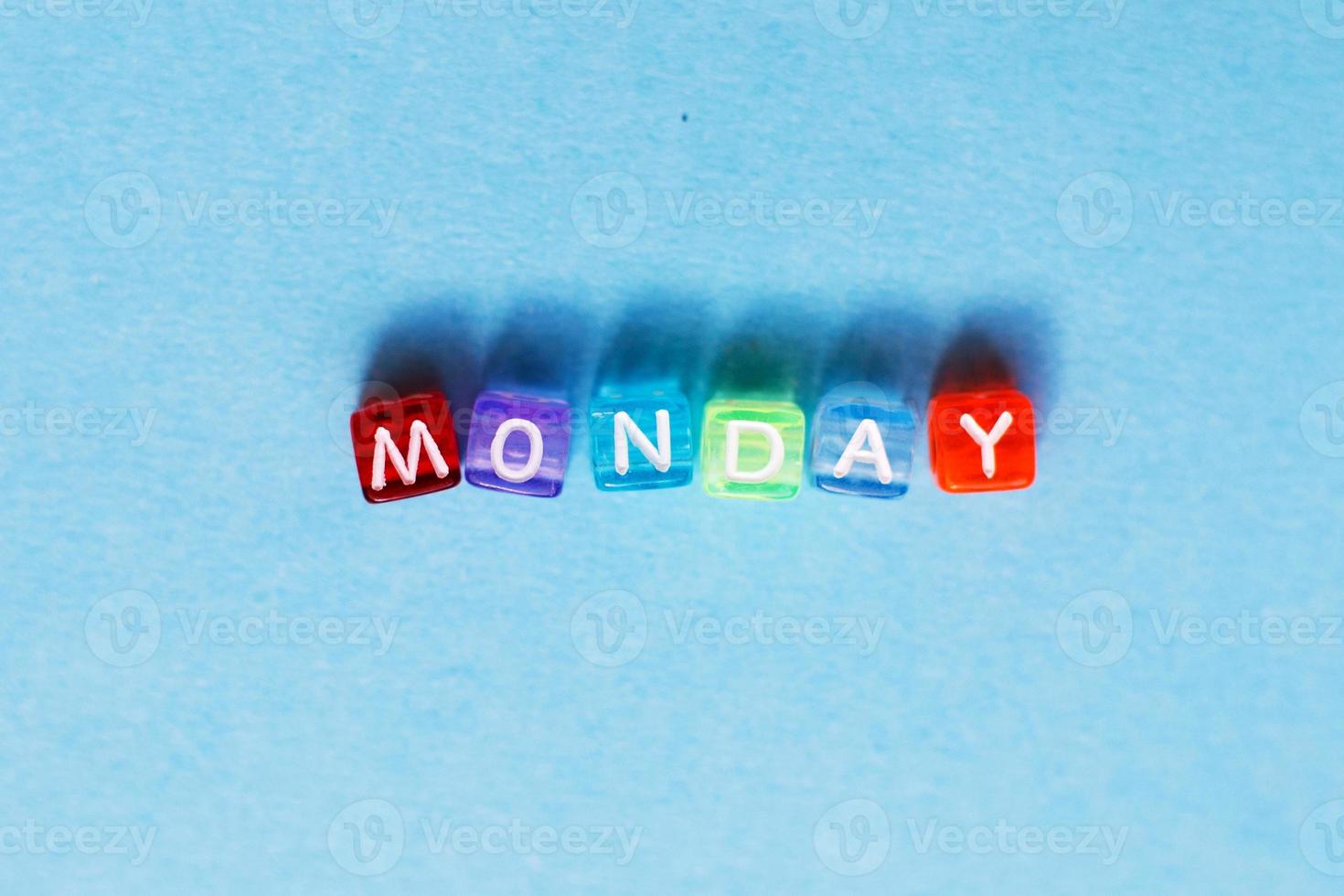 inskrift måndag tillverkad förbi Flerfärgad plast kuber på en blå bakgrund. foto