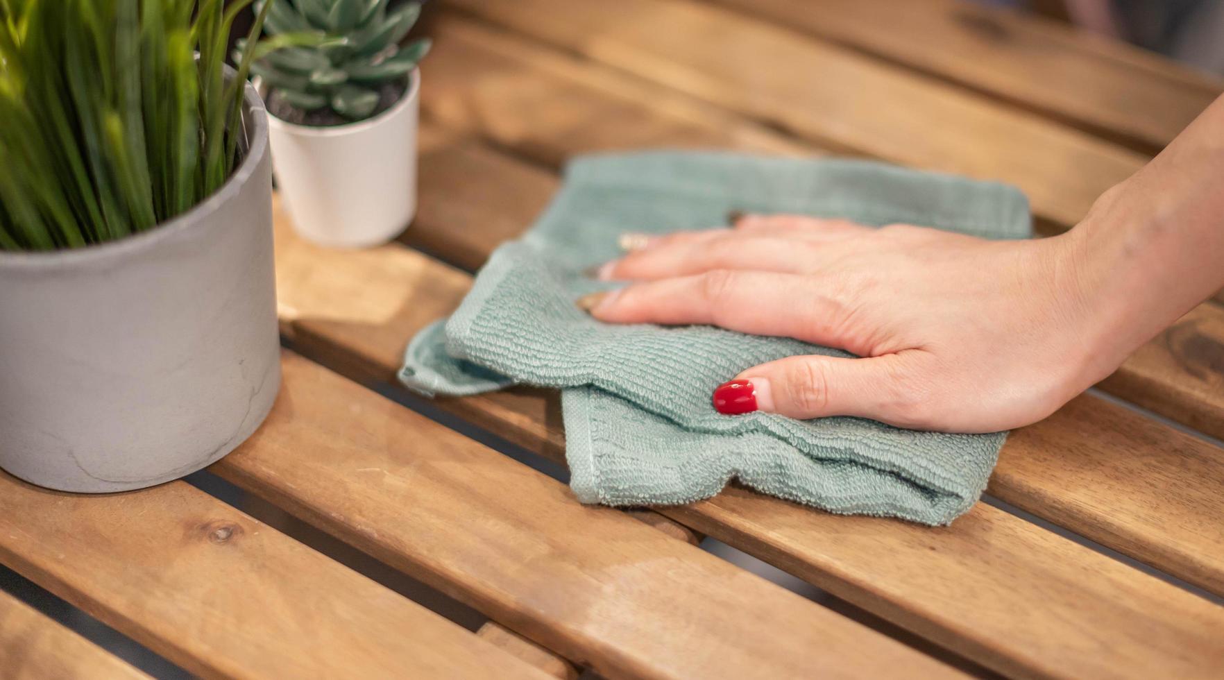 stänga upp kvinna hand rengöring trä- tabell använder sig av desinfektionsmedel grön handduk. förhindra infektion av covid-19 virus, förorening av bakterier eller bakterie, torka eller rengöring till eliminera. foto