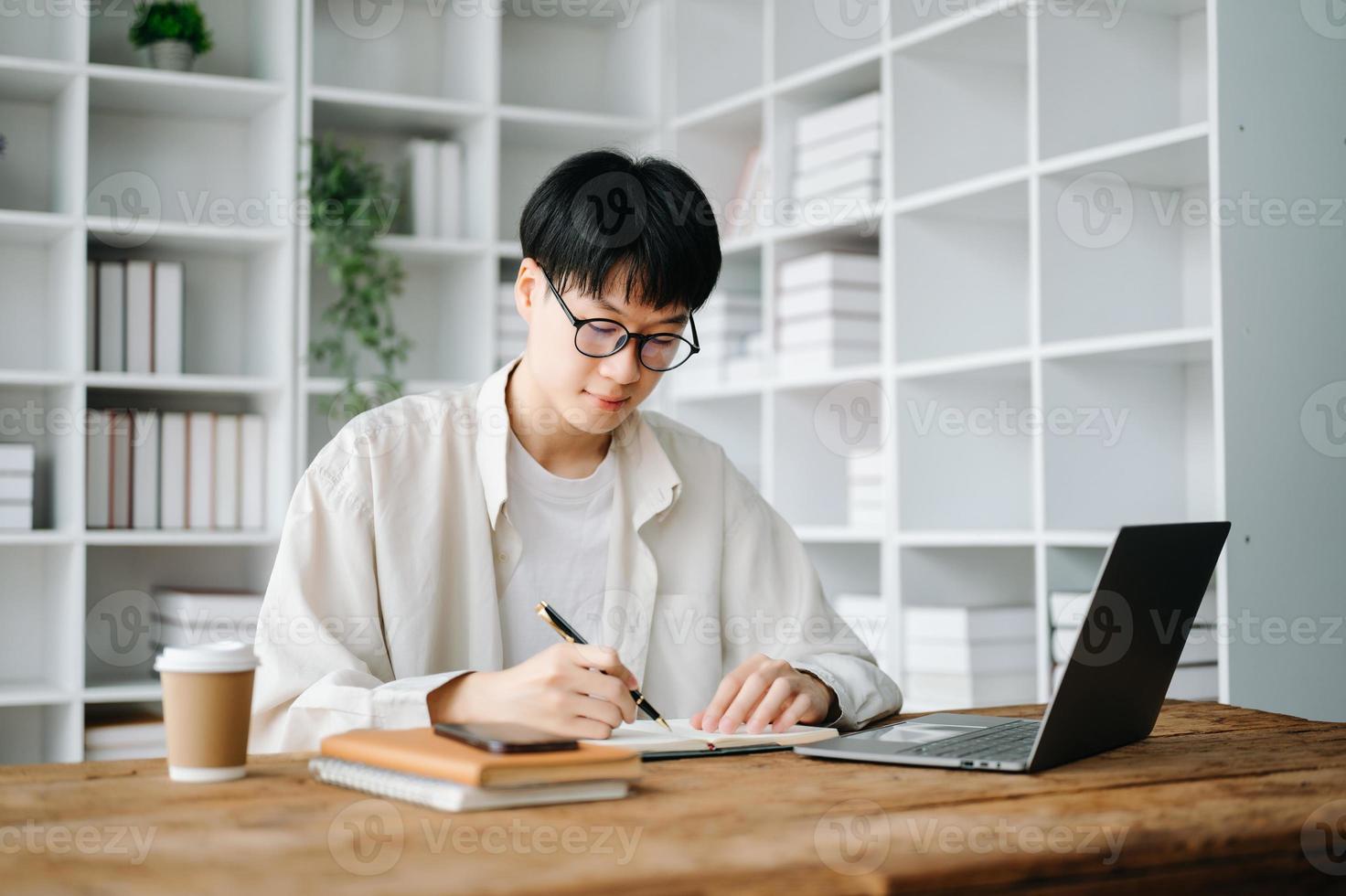 stilig och begåvad ung asiatisk man studerande arbetssätt på hans projekt uppdrag, använder sig av bärbar dator och läsplatta till Sök ett uppkopplad information. foto