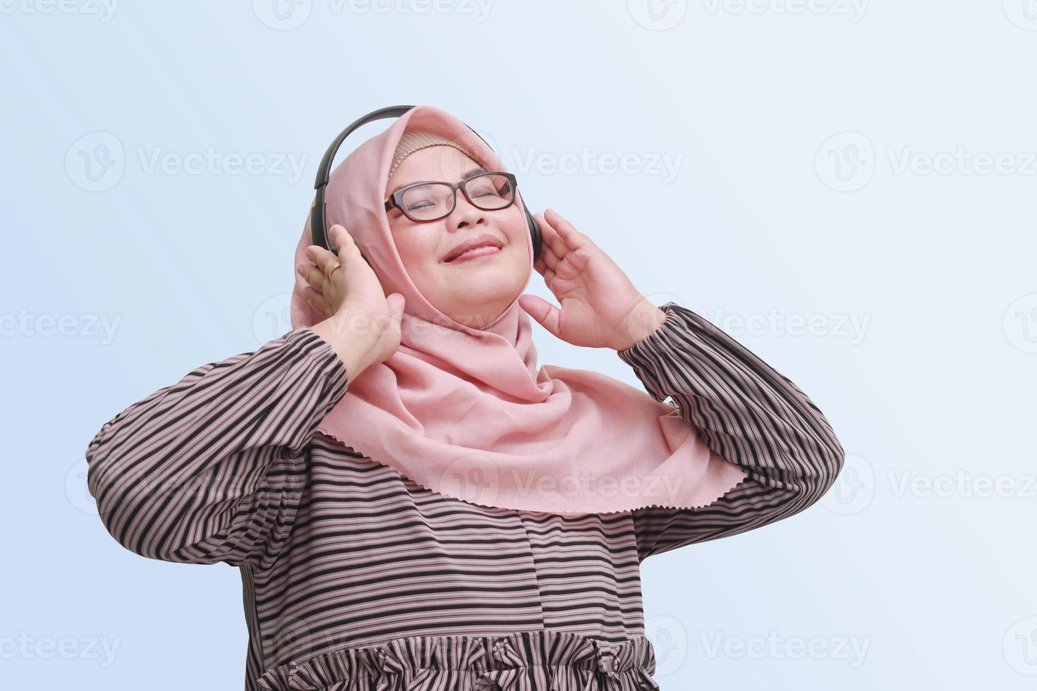 porträtt av glad asiatisk kvinna med hijab, njuter och lyssnande till musik använder sig av hörlurar. isolerat bild på blå bakgrund foto
