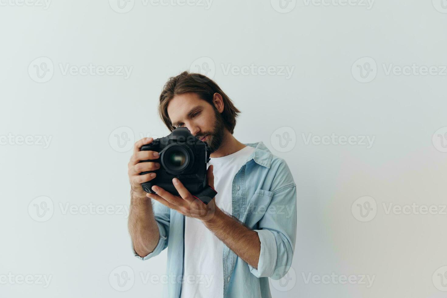 man hipster fotograf i en studio mot en vit bakgrund innehav en professionell kamera och miljö den upp innan skytte. livsstil arbete som en frilans fotograf foto