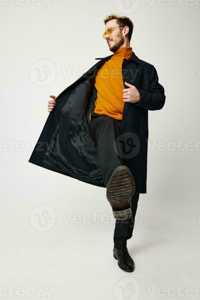 söt kille i ett orange Tröja knäppte upp täcka byxor modell ljus bakgrund foto
