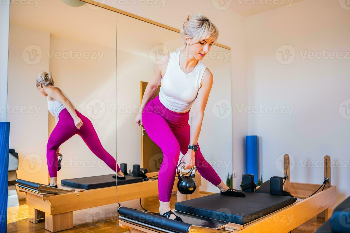 blond kvinna är utövar på pilates reformator säng i henne Hem. foto