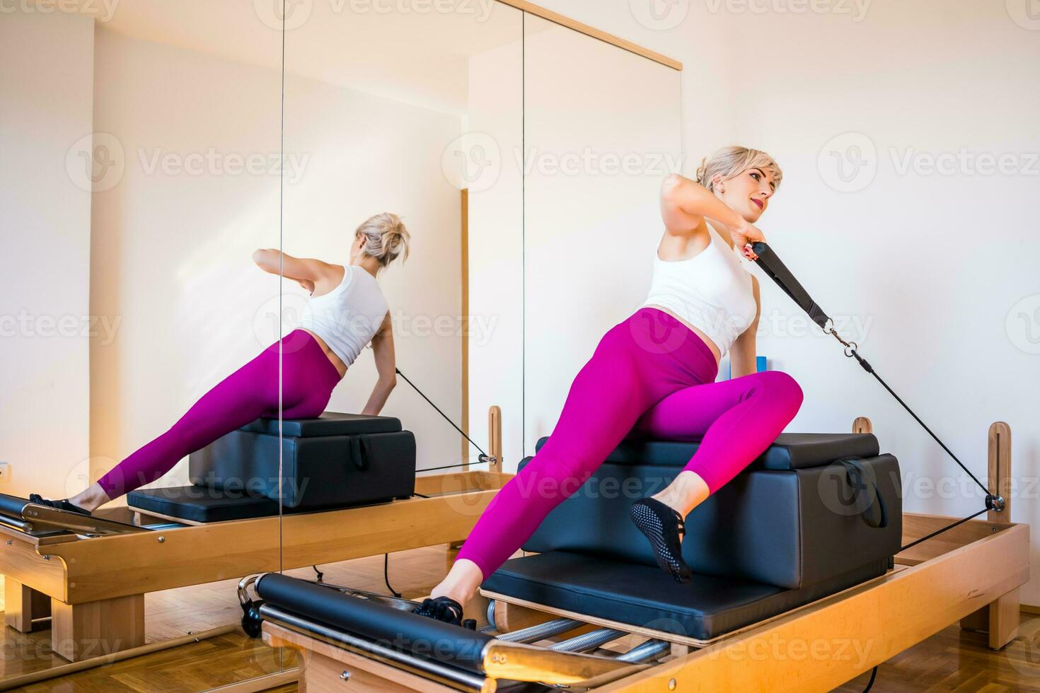 blond kvinna är utövar på pilates reformator säng i henne Hem. foto